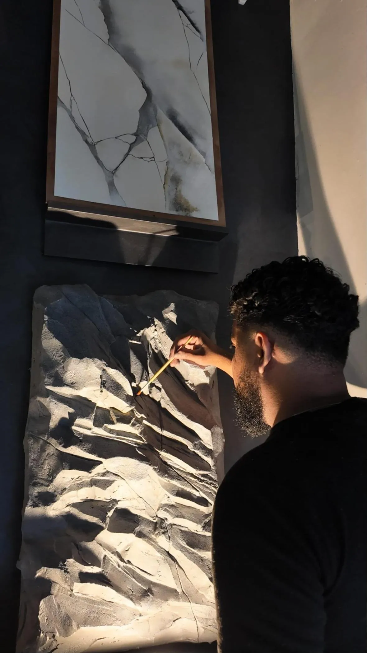 Paulinho pintando com pincel um painel de rocha esculpida, sob um quadro de efeito mármore
