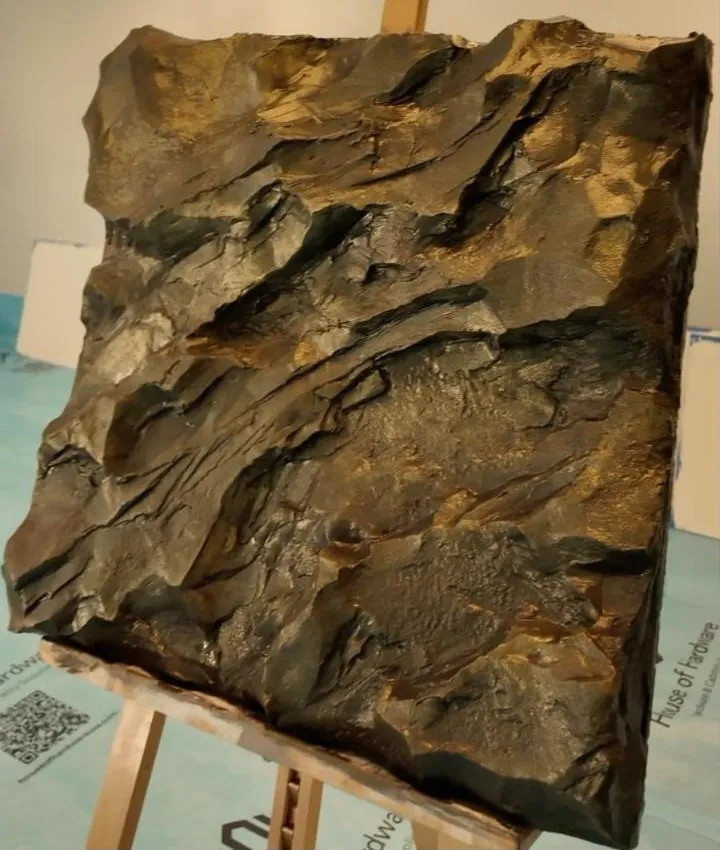 Painel de rocha esculpida com acabamento escuro e bronze, sobre cavalete