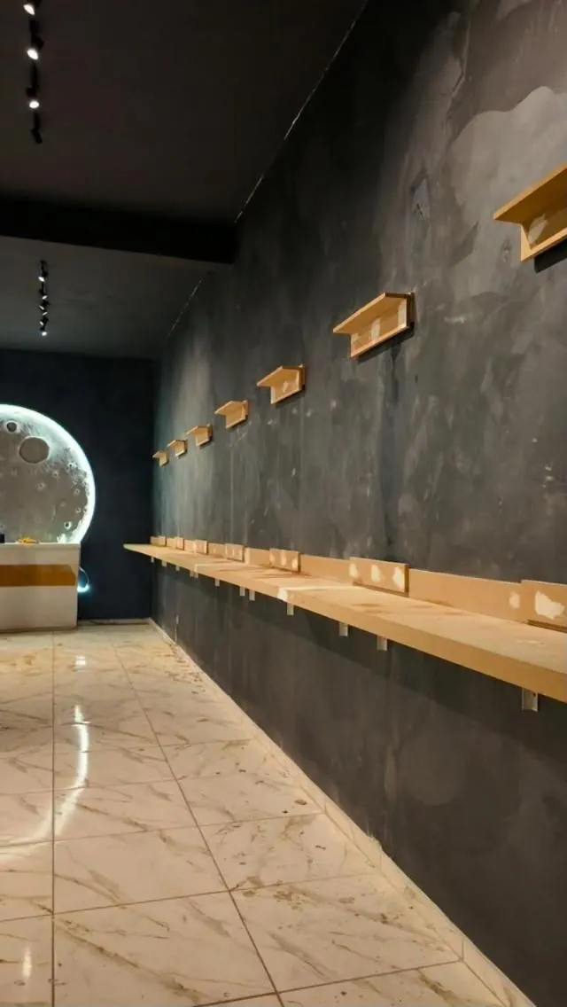 Interior do estúdio: parede grafite com prateleiras de amostras e painel de Lua ao fundo