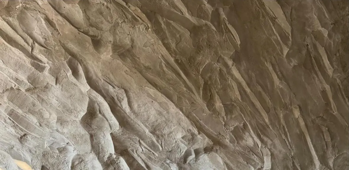 Textura de rocha clara esculpida à mão, com relevo marcado em luz rasante